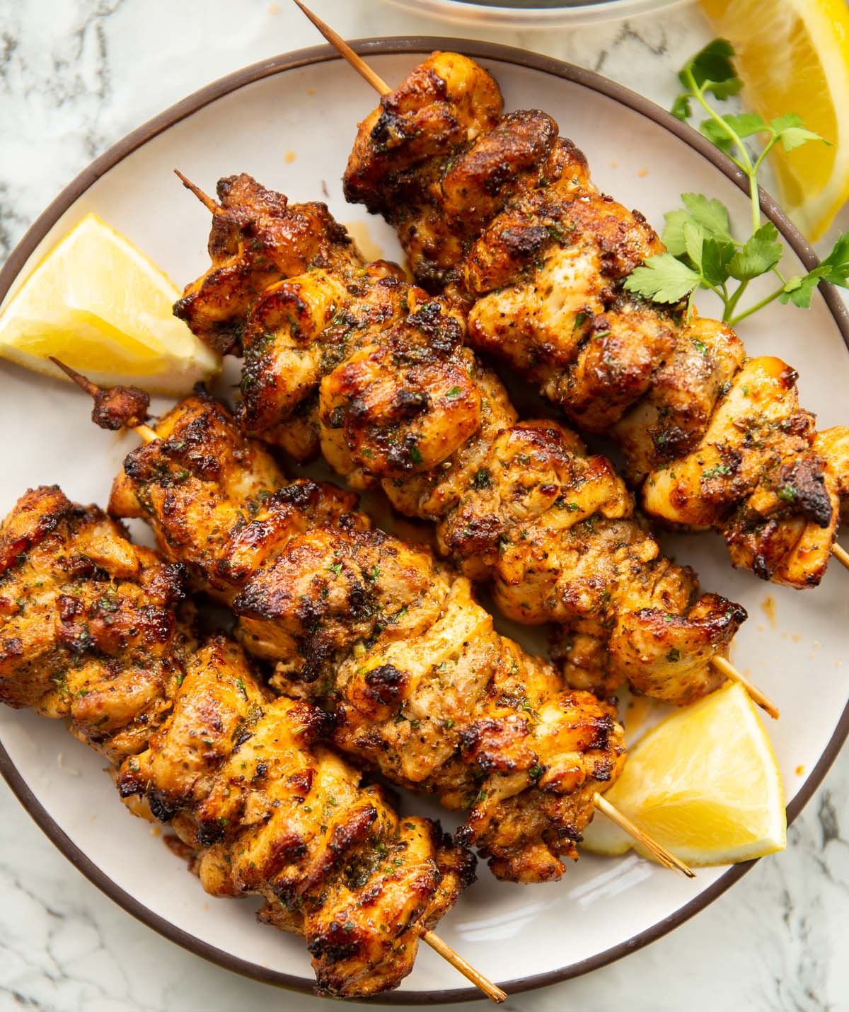 four lemon butter chicken skewers on small white plate