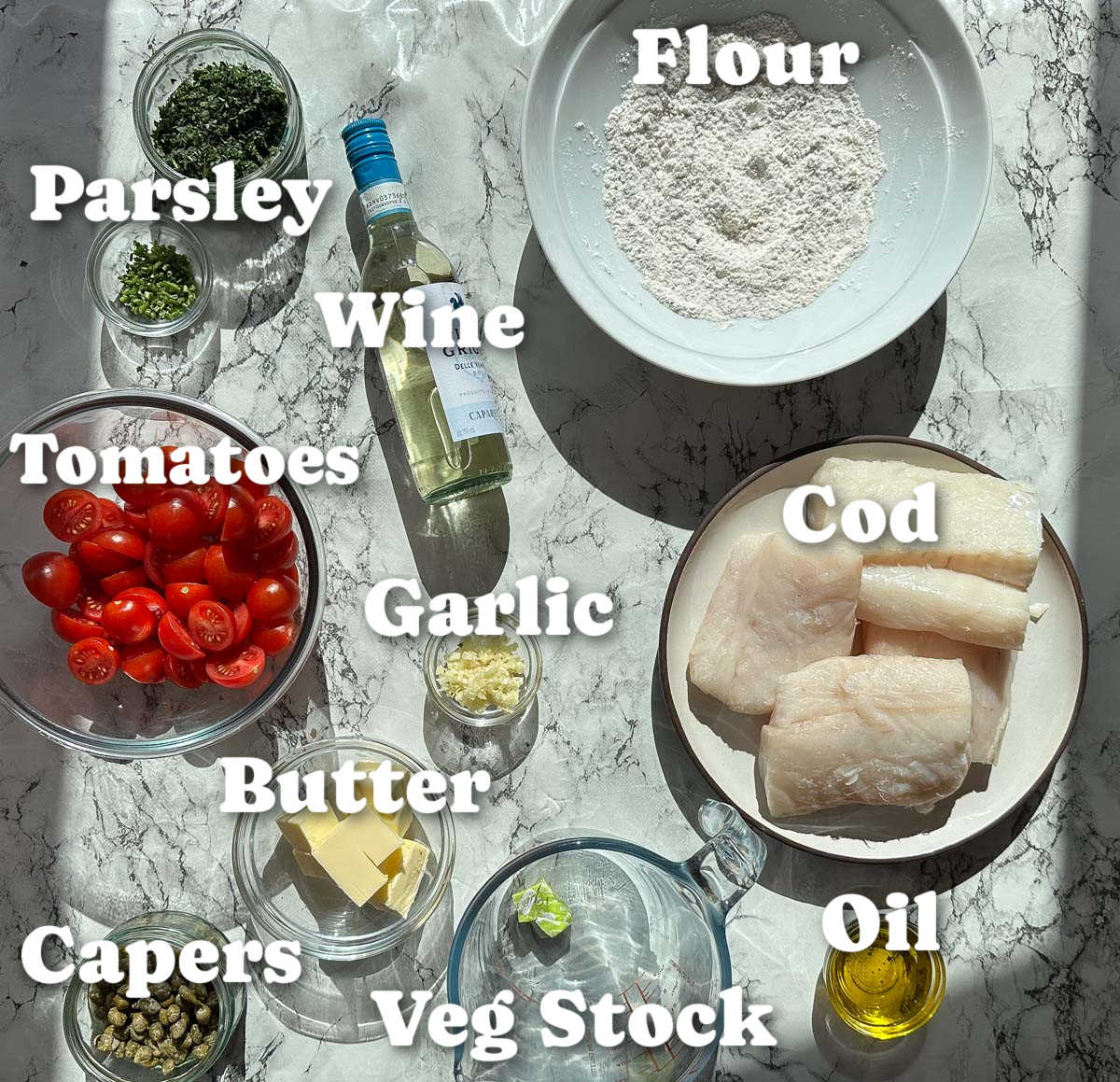 overhead shot of cod with tomatoes and capers ingredients with text labels