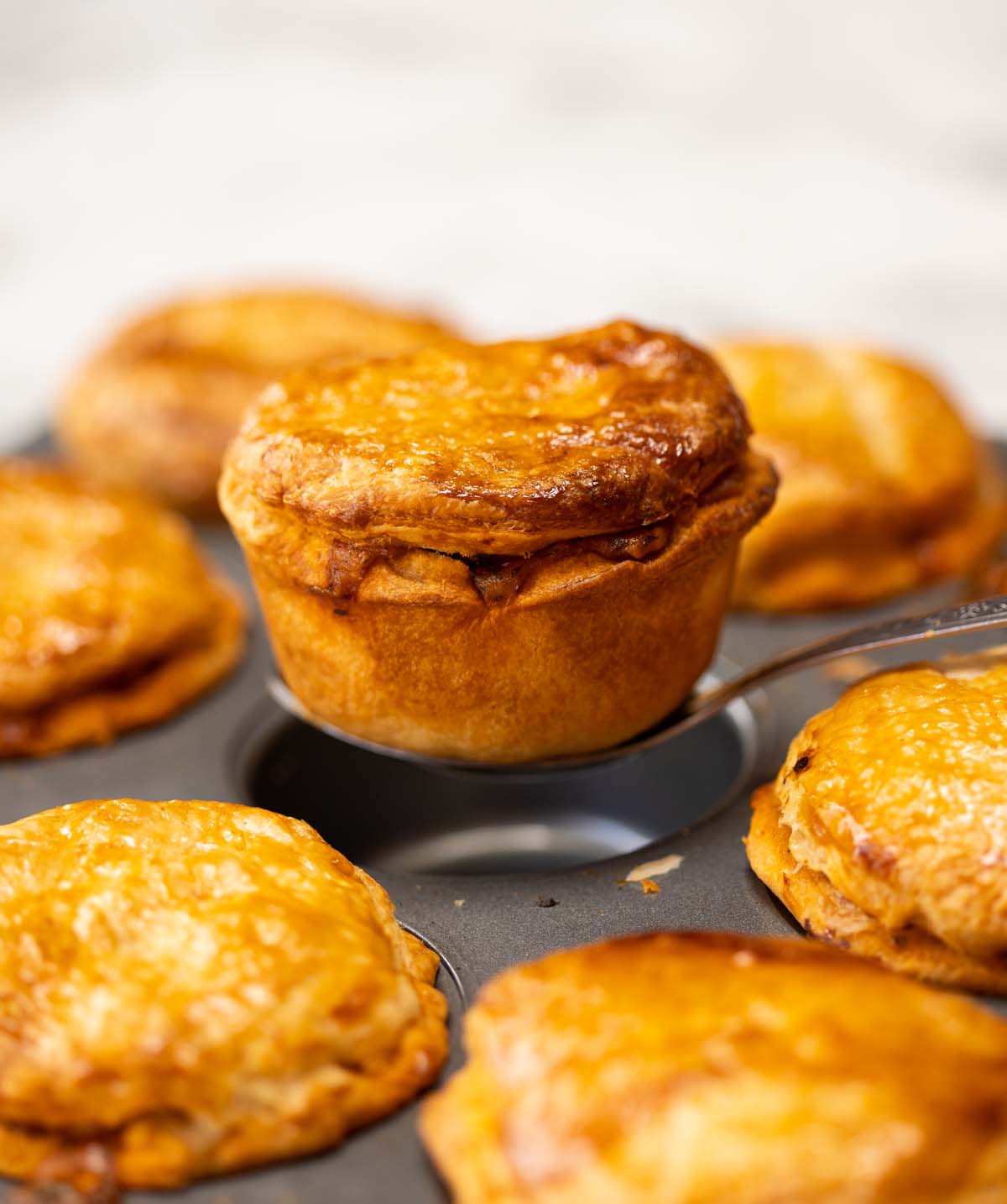 silver spoon lifting mini chicken chorizo pie out of tray