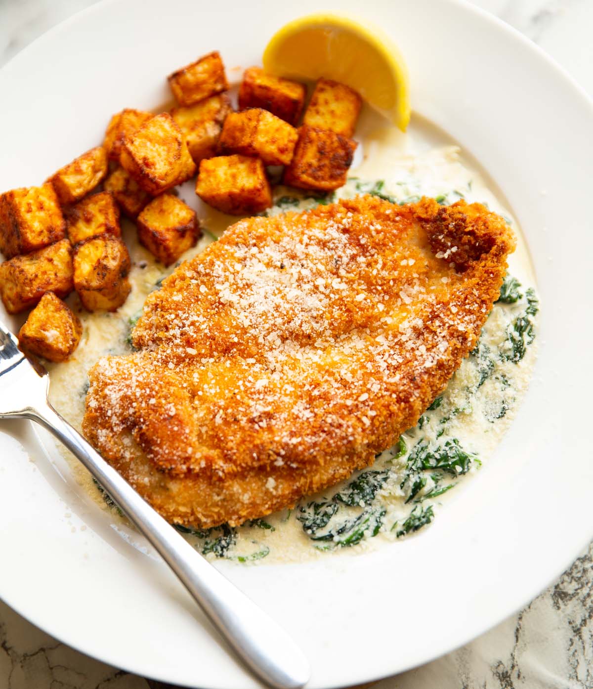 chicken and creamed spinach on white plate with potatoes and silver fork