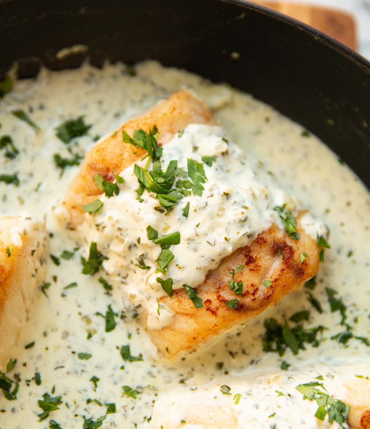 creamy parsley cod in pan garnished with extra parsley