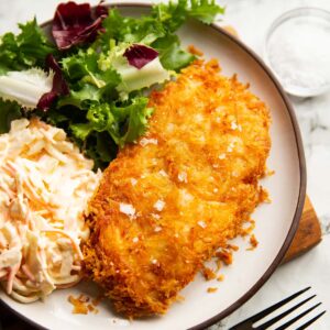hash brown chicken served on small white plate with salad and coleslaw